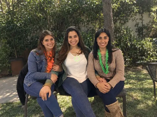 Cote con sus dos hermanas, sentadas en una banca de jardín
