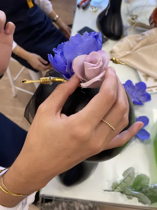Manos arman flores de tela moradas y rosadas sobre un tocado