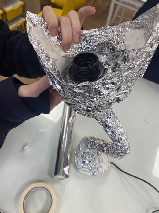 Manos sostienen un prototipo de lámpara hecho con papel aluminio y un portalámparas