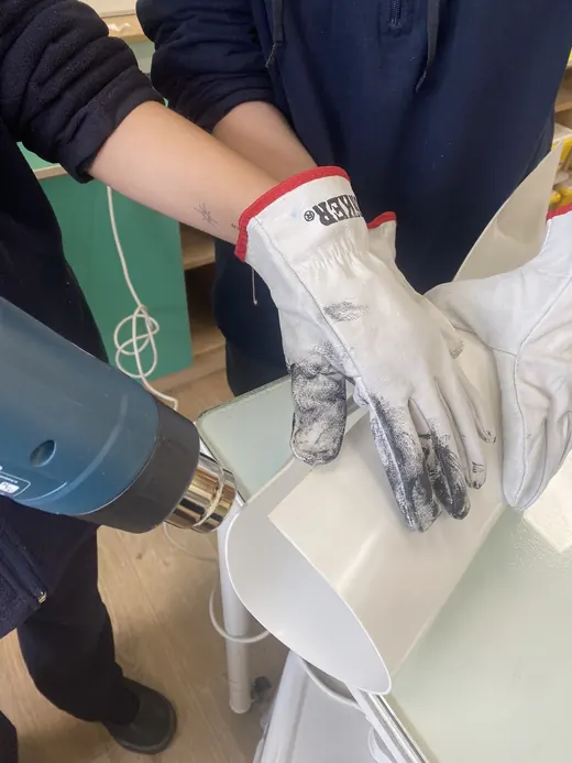 Manos con guantes doblan una lámina blanca con una pistola de calor